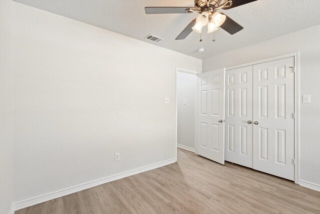 unfurnished bedroom with light wood-type flooring, a textured ceiling, ceiling fan, and a closet