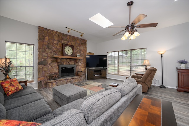 living room with a skylight, ceiling fan, rail lighting, a stone fireplace, and wood-type flooring