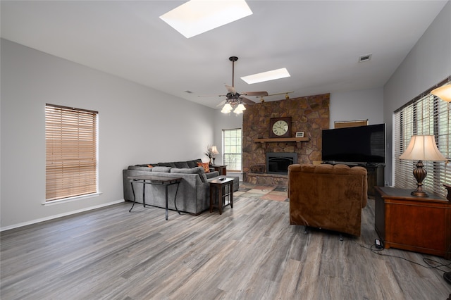 living room with a skylight, ceiling fan, hardwood / wood-style floors, and a fireplace