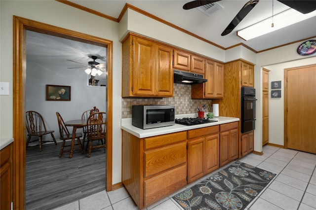 kitchen with black appliances, backsplash, light tile patterned floors, and crown molding