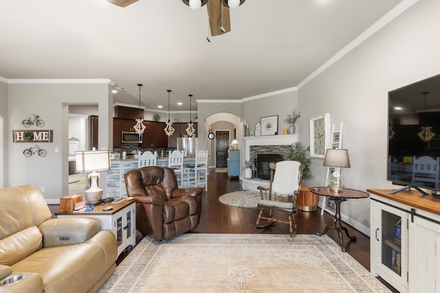 living room featuring crown molding, ceiling fan, wood-type flooring, and a fireplace