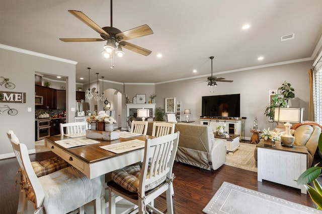 dining space featuring crown molding, dark wood-type flooring, ceiling fan, and a fireplace