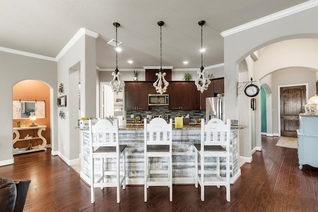 kitchen with dark brown cabinets, light stone counters, hanging light fixtures, dark hardwood / wood-style floors, and appliances with stainless steel finishes