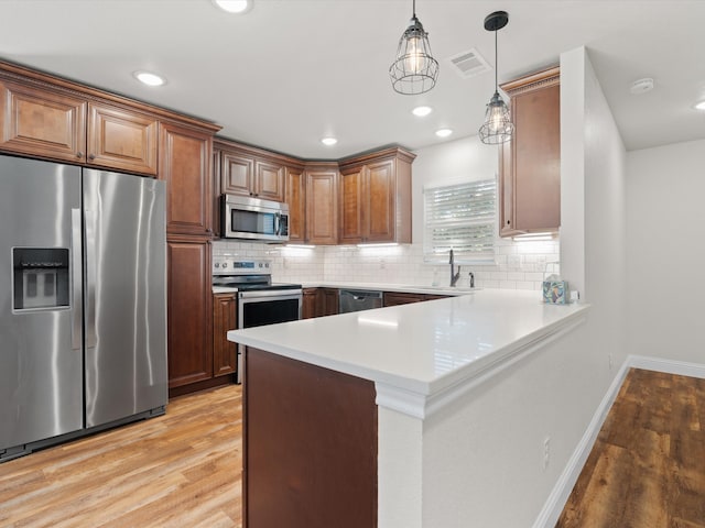 kitchen with light wood-type flooring, decorative light fixtures, stainless steel appliances, and kitchen peninsula