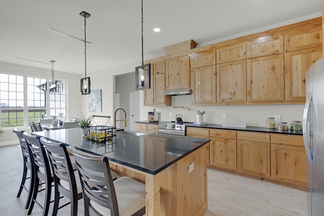 kitchen with a breakfast bar area, appliances with stainless steel finishes, light brown cabinetry, under cabinet range hood, and a sink