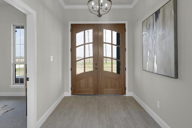 entrance foyer with ornamental molding, french doors, a chandelier, and light hardwood / wood-style flooring