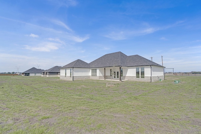 rear view of property featuring stone siding, a shingled roof, fence, and a lawn