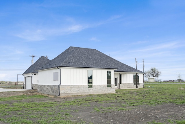 view of side of home with a shingled roof, concrete driveway, a lawn, a garage, and stone siding