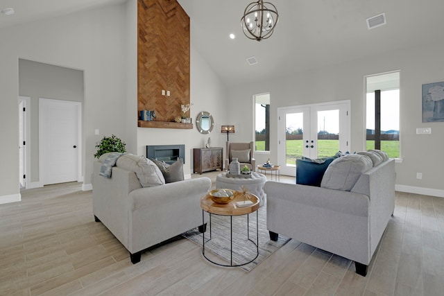 living room with high vaulted ceiling, an inviting chandelier, light hardwood / wood-style floors, and french doors