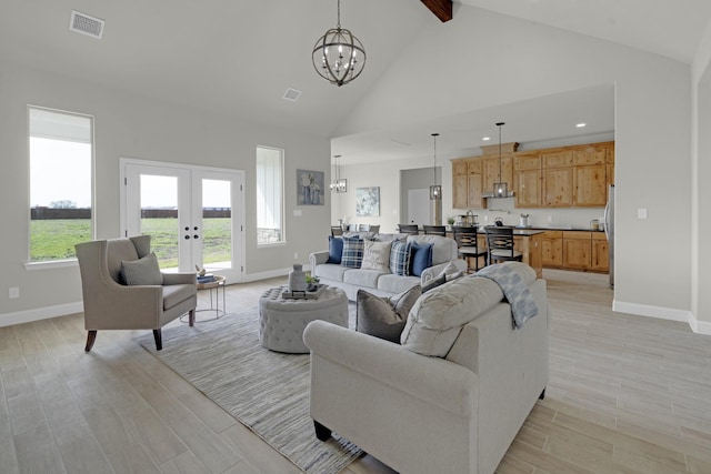 living area with high vaulted ceiling, light wood-style floors, visible vents, and a notable chandelier