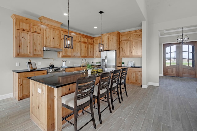 kitchen with appliances with stainless steel finishes, light brown cabinets, an island with sink, pendant lighting, and a breakfast bar