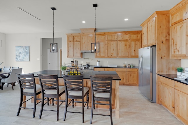 kitchen with a center island with sink, pendant lighting, light brown cabinetry, light hardwood / wood-style floors, and stainless steel refrigerator