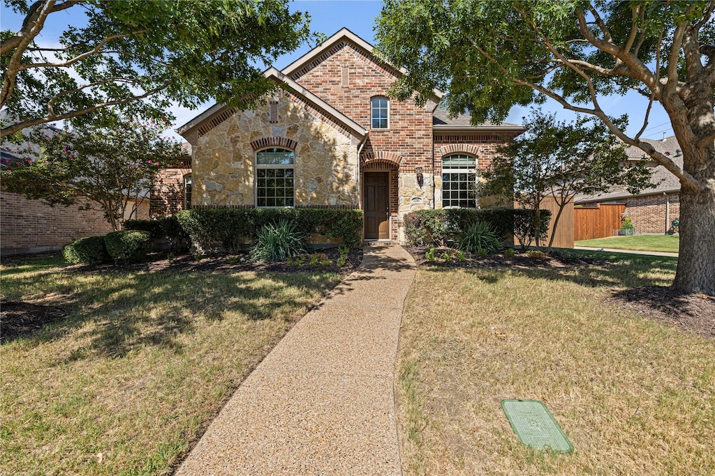 view of front of property featuring stone siding, a front yard, fence, and brick siding