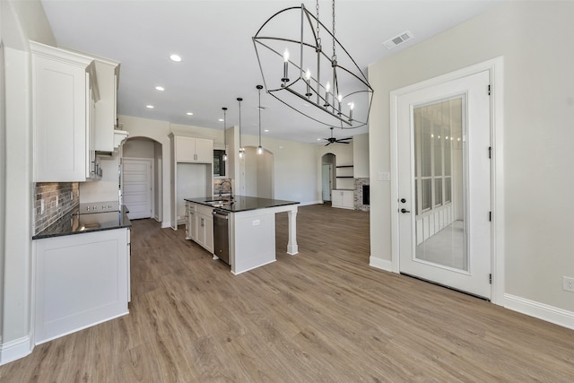 kitchen with hanging light fixtures, light hardwood / wood-style flooring, decorative backsplash, a center island with sink, and stainless steel dishwasher