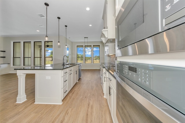 kitchen featuring light wood-type flooring, pendant lighting, white cabinetry, a kitchen bar, and an island with sink