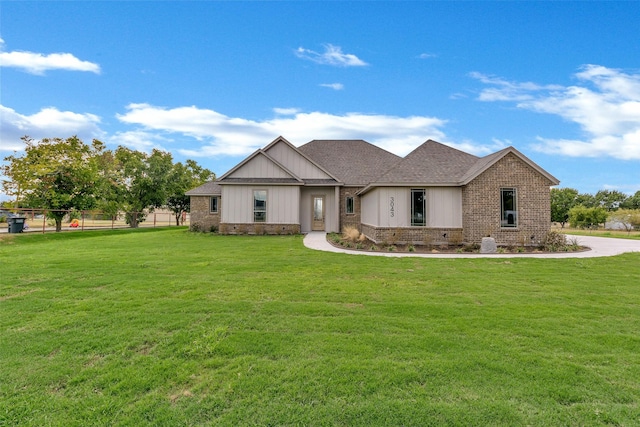 view of front of house featuring brick siding, roof with shingles, a front lawn, and fence