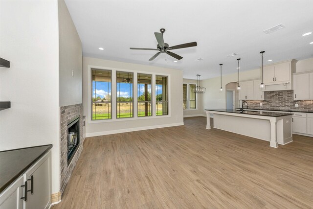 unfurnished living room featuring a fireplace, sink, ceiling fan, and light hardwood / wood-style floors