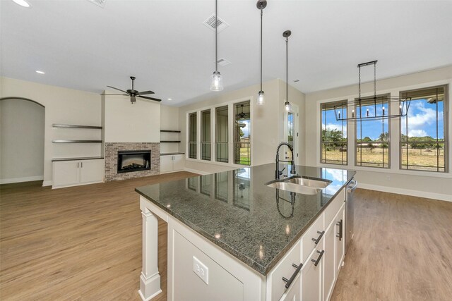 kitchen with a fireplace, dark stone countertops, white cabinetry, an island with sink, and sink