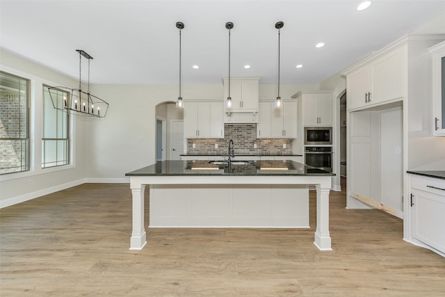 kitchen featuring light wood-type flooring, white cabinetry, a center island with sink, and stainless steel oven