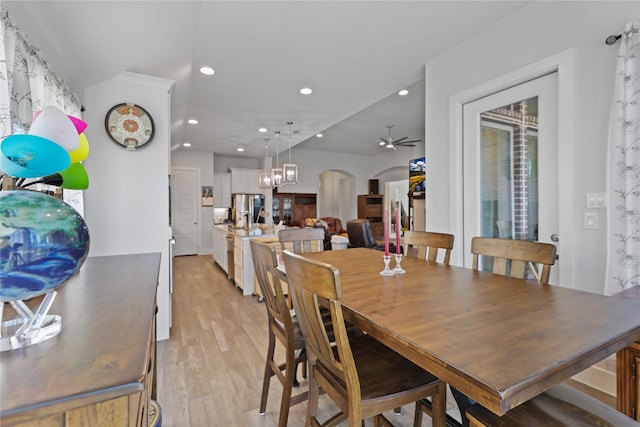 dining area with arched walkways, recessed lighting, light wood-style flooring, and ceiling fan with notable chandelier