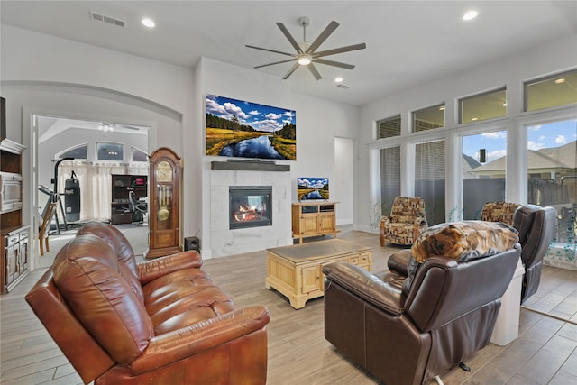 living room featuring a ceiling fan, visible vents, arched walkways, a tile fireplace, and light wood-type flooring