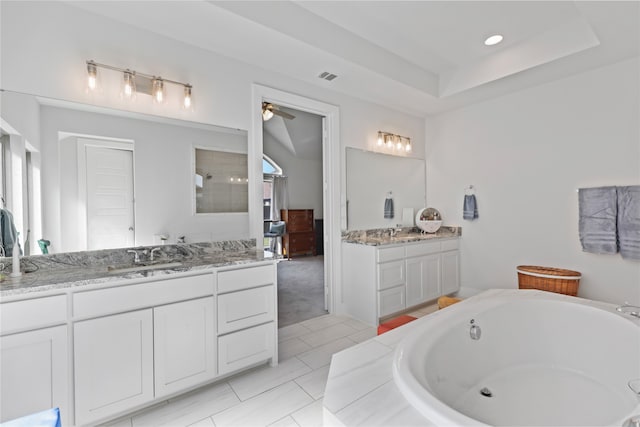 bathroom featuring visible vents, a garden tub, two vanities, a sink, and a raised ceiling