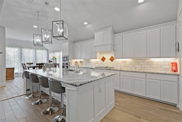 kitchen with a sink, stainless steel appliances, white cabinets, light wood finished floors, and decorative backsplash