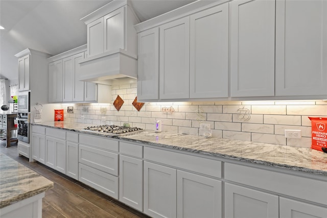 kitchen featuring light stone counters, dark wood finished floors, appliances with stainless steel finishes, white cabinets, and decorative backsplash