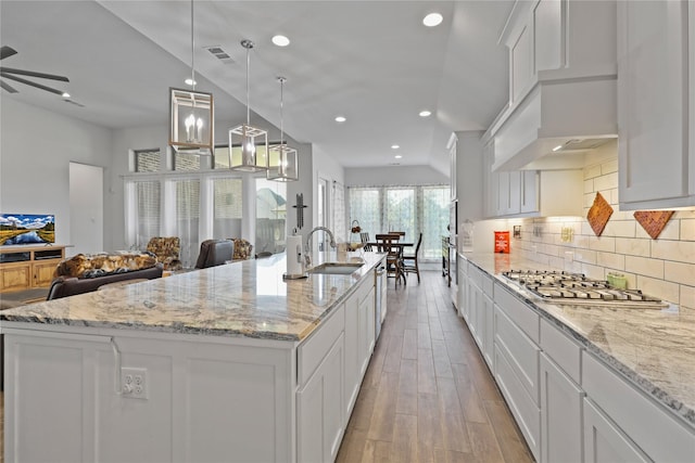 kitchen with light wood finished floors, open floor plan, decorative backsplash, appliances with stainless steel finishes, and a sink