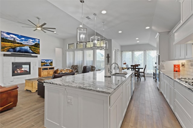 kitchen featuring pendant lighting, white cabinetry, sink, light stone counters, and a center island with sink