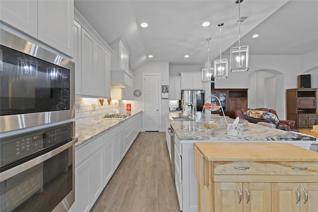 kitchen featuring appliances with stainless steel finishes, white cabinetry, hanging light fixtures, a kitchen island with sink, and light brown cabinets