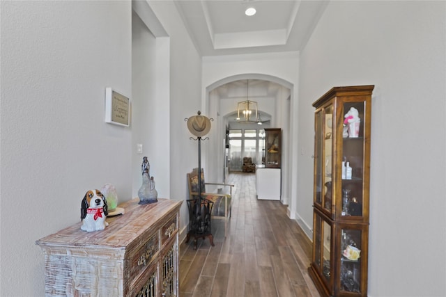 hallway with a tray ceiling, baseboards, arched walkways, and dark wood-style floors