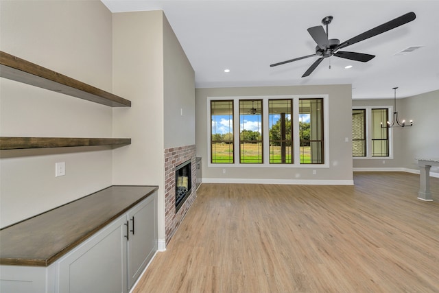 unfurnished living room featuring ceiling fan with notable chandelier, a fireplace, and light hardwood / wood-style floors