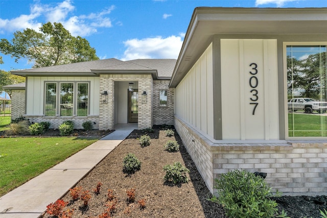 view of exterior entry featuring a yard, brick siding, and board and batten siding