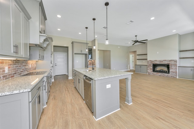 kitchen with light wood-type flooring, a brick fireplace, light stone counters, sink, and ceiling fan