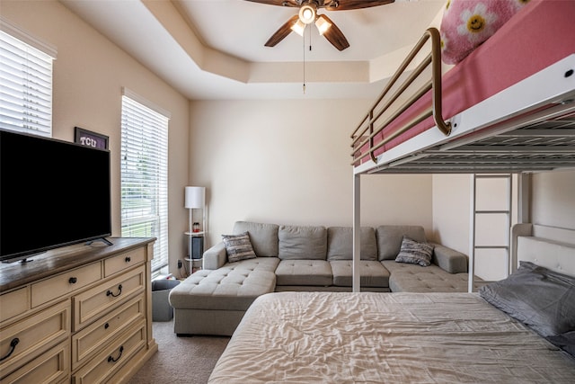 carpeted bedroom featuring a tray ceiling and ceiling fan