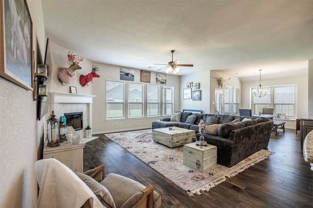 living room with ceiling fan with notable chandelier, a tiled fireplace, dark hardwood / wood-style floors, and a textured ceiling