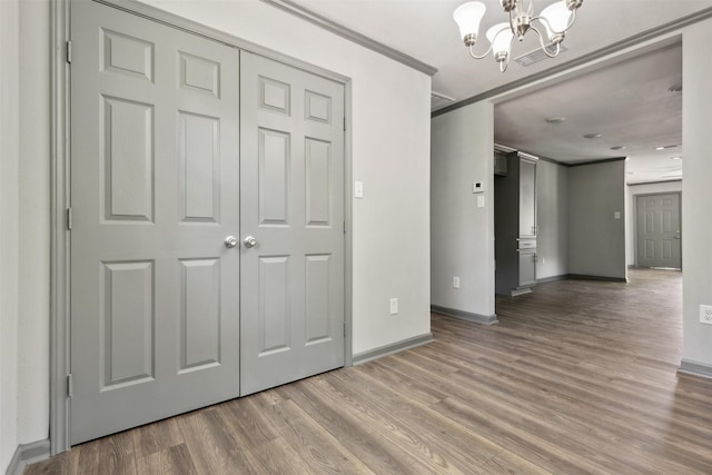 unfurnished bedroom with baseboards, ornamental molding, wood finished floors, a chandelier, and a closet