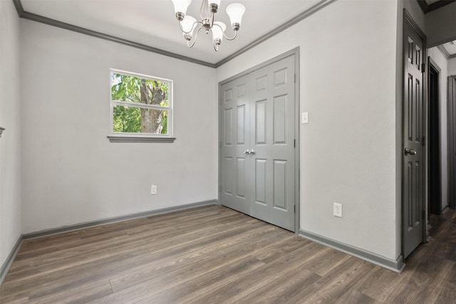 unfurnished bedroom with baseboards, ornamental molding, wood finished floors, an inviting chandelier, and a closet