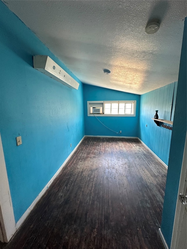 empty room featuring dark wood-type flooring, cooling unit, lofted ceiling, and a textured ceiling