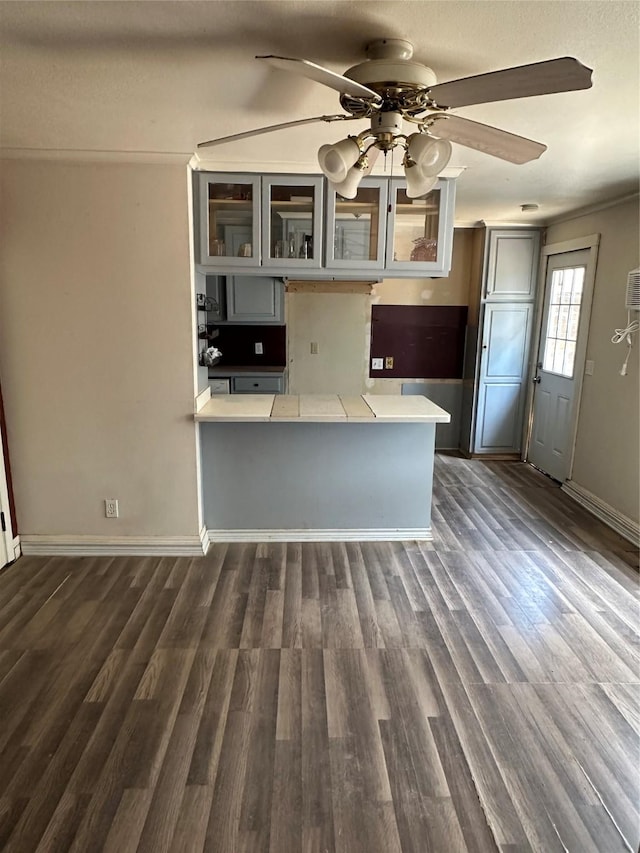 kitchen featuring glass insert cabinets, ceiling fan, light countertops, a peninsula, and dark wood-style floors