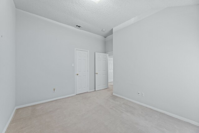 unfurnished room featuring lofted ceiling, light carpet, and a textured ceiling