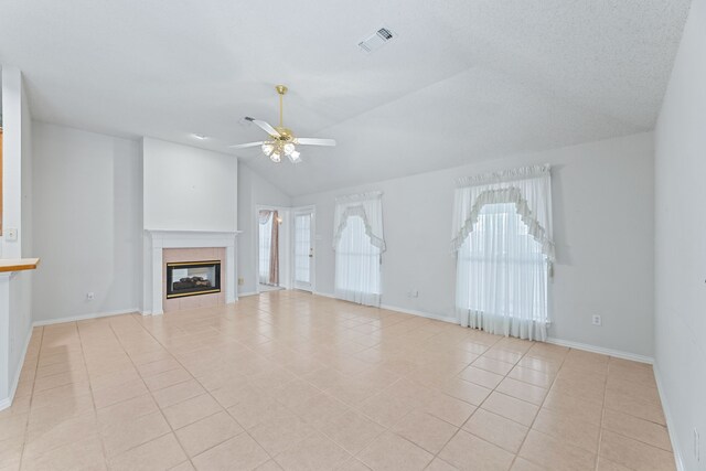 unfurnished living room with a textured ceiling, vaulted ceiling, a tile fireplace, light tile patterned floors, and ceiling fan