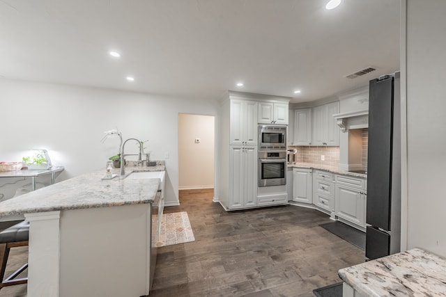 kitchen with white cabinetry, appliances with stainless steel finishes, dark hardwood / wood-style floors, decorative backsplash, and a breakfast bar area