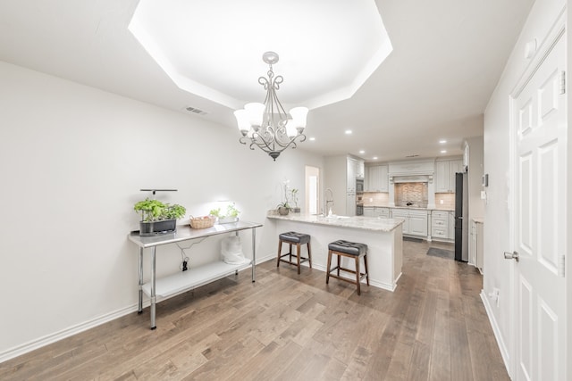 kitchen featuring a peninsula, wood finished floors, freestanding refrigerator, decorative backsplash, and a raised ceiling