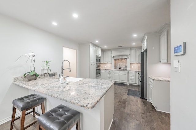 kitchen with backsplash, appliances with stainless steel finishes, a sink, a peninsula, and a kitchen bar