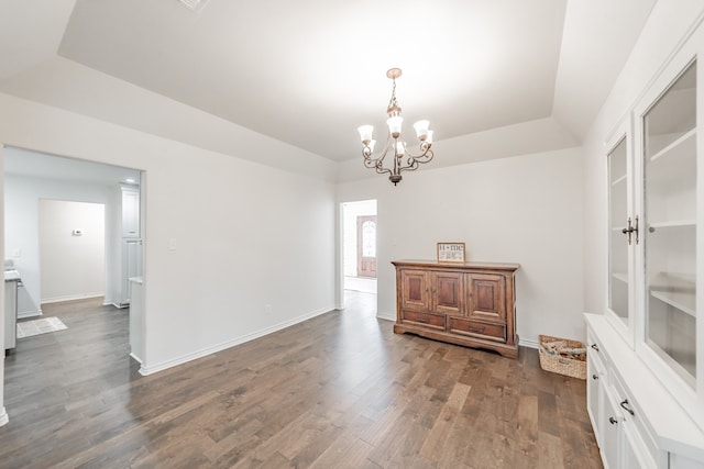 dining area with a tray ceiling, a notable chandelier, dark wood finished floors, and baseboards