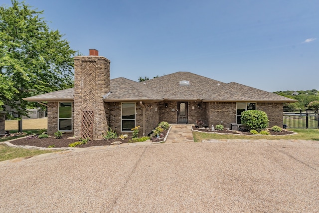 view of front of property with a shingled roof, a chimney, fence, and brick siding