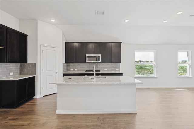 kitchen with a center island with sink, light hardwood / wood-style flooring, stainless steel appliances, and vaulted ceiling