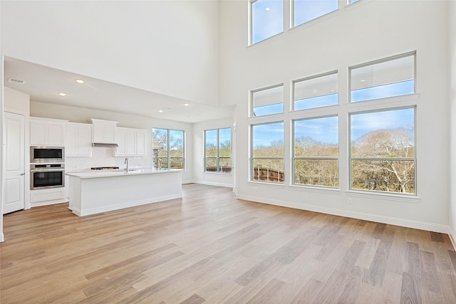 unfurnished living room featuring a high ceiling, light hardwood / wood-style flooring, and sink